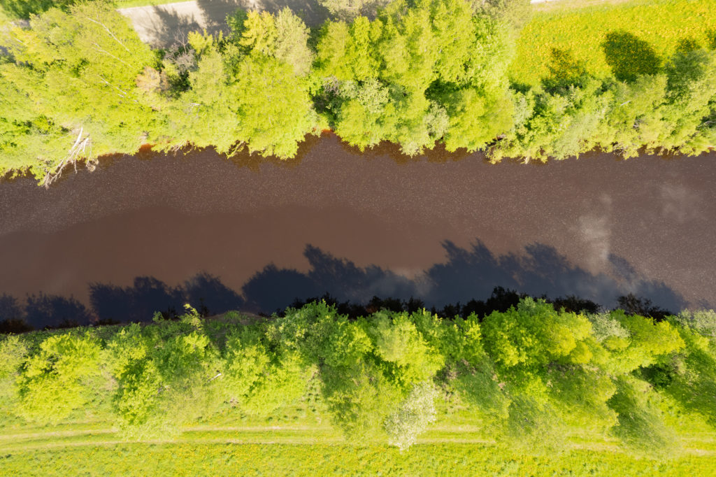 Kuvituskuva Limingan Vesihuollon nettisivujen Tietoa hulevedestä -alasivulla, jonka aiheena on hulevesi. Kuvassa ilmasta käsin otettu kuva joesta ja sen vihreistä penkoista.